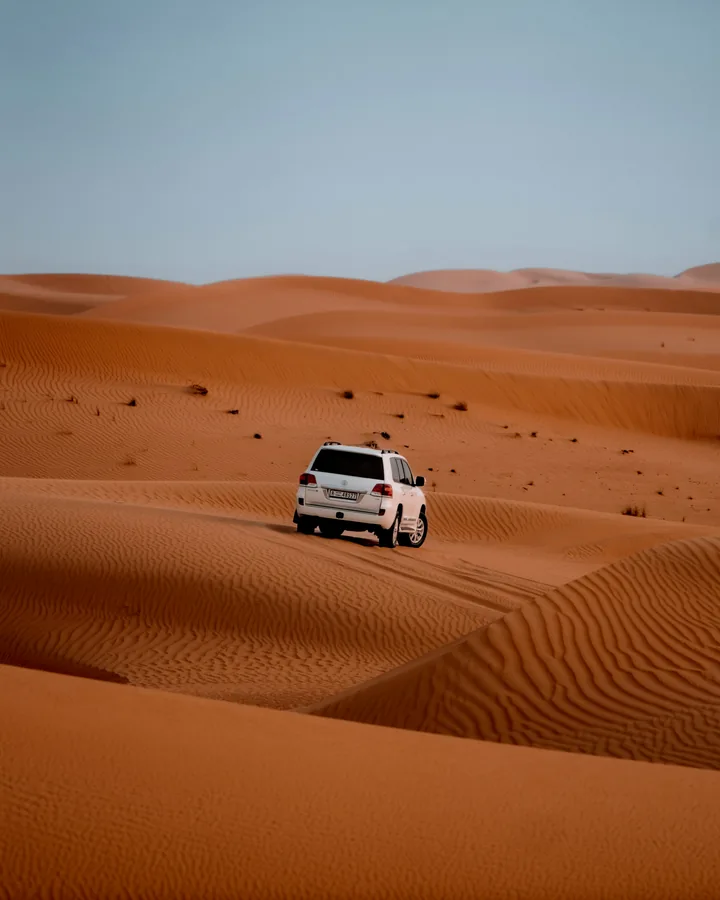 A vehicle travelling across orange sand dunes, shown as representative desert safari photography