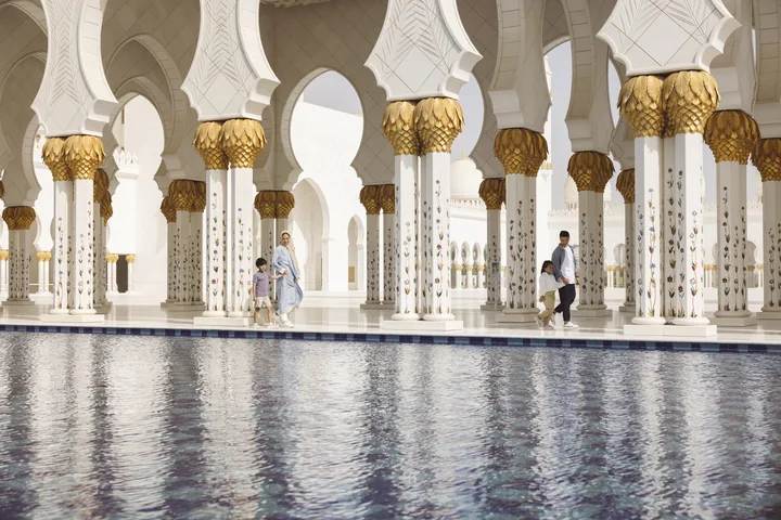 White marble arches and gold column capitals beside a reflecting pool at Sheikh Zayed Grand Mosque